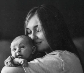 Woman holds a small baby close against her shoulder in a quiet, softly lit setting