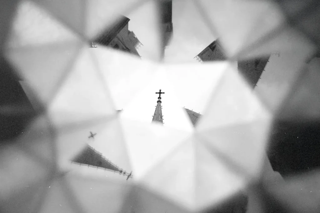 A church steeple topped with a cross is reflected and multiplied through a kaleidoscope‑like pattern of geometric shapes
