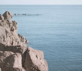 Rocky shoreline overlooking a calm blue sea with a distant sailboat on the horizon