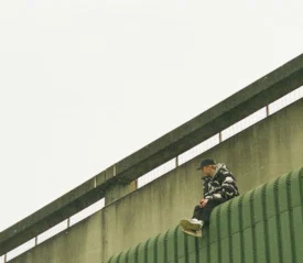Silhouetted figure standing at the top of a walkway lined with tall flagpoles under a hazy evening sky