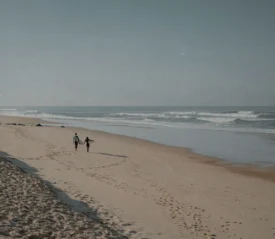 Couple walking along an empty sandy beach beside gentle ocean waves
