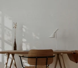 andinavian-style workspace featuring a wooden desk, simple chair, white lamp, and dried botanicals with sunlight filtering through a nearby window