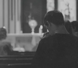 A dimly lit interior of a church where a person sits in a pew facing the altar