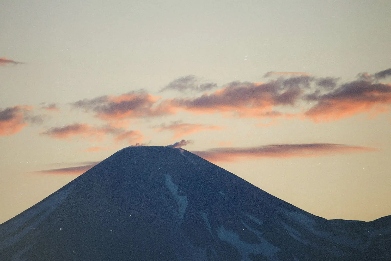 Snow‑covered mountain peak at sunrise with soft pink clouds drifting across the sky