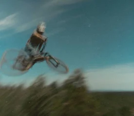 A cyclist performs a high jump on a mountain bike, captured in a motion‑blurred scene against a blue sky