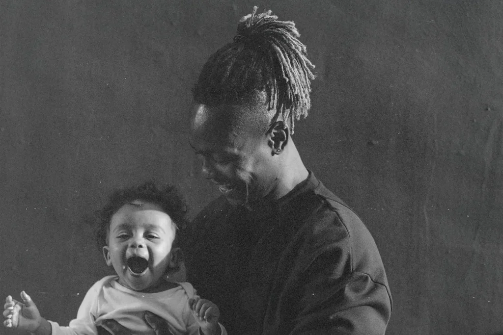A man smiles while holding a small child in his arms in a softly lit, monochrome portrait