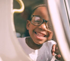 A child sits by a window on a vehicle, resting a hand on the window frame while looking outside