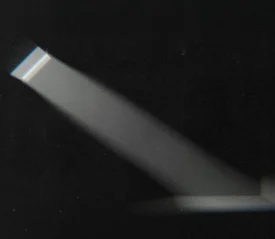 A narrow beam of light shines through a small window or opening, cutting across a dark room and illuminating a portion of the wall and floor