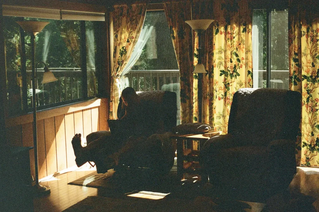 Cozy living room with patterned curtains and large windows, where someone sits in a recliner next to soft natural light