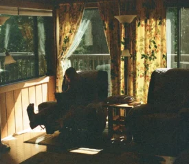 Cozy living room with patterned curtains and large windows, where someone sits in a recliner next to soft natural light