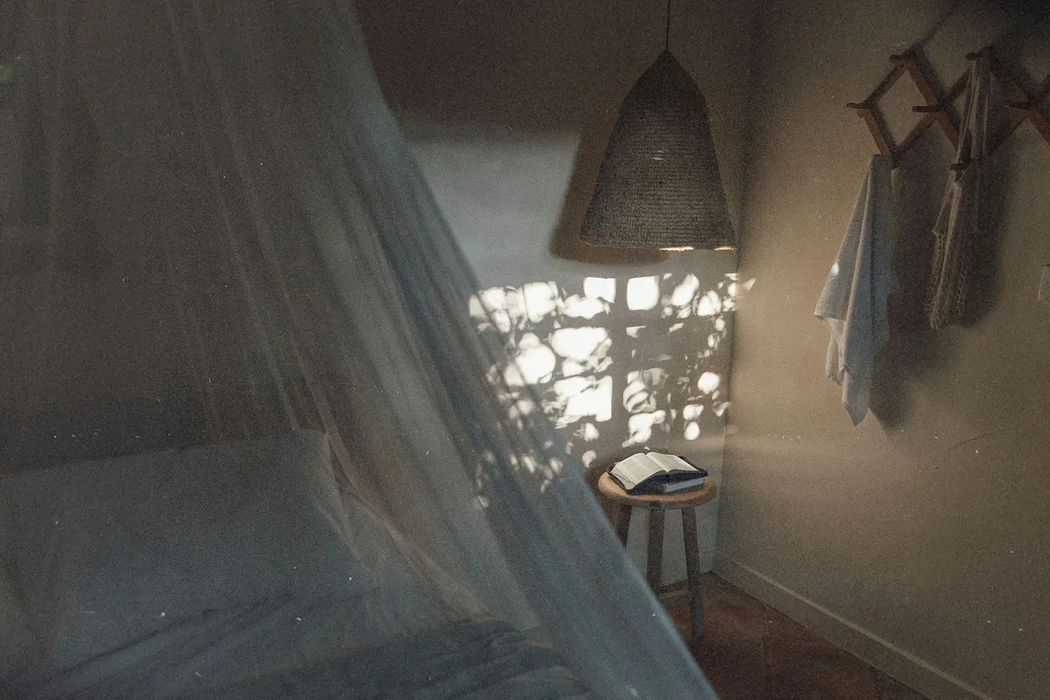 Soft morning light filters through a window into a cozy bedroom, illuminating an open book on a small wooden stool