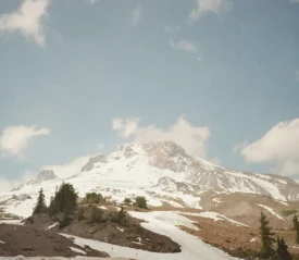 A snow‑covered mountain rises beneath a bright blue sky with scattered white clouds
