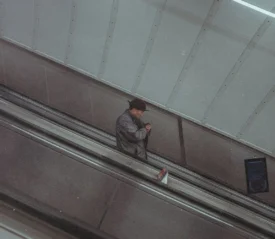 A person rides down an escalator inside a modern building with metal panels and overhead lighting