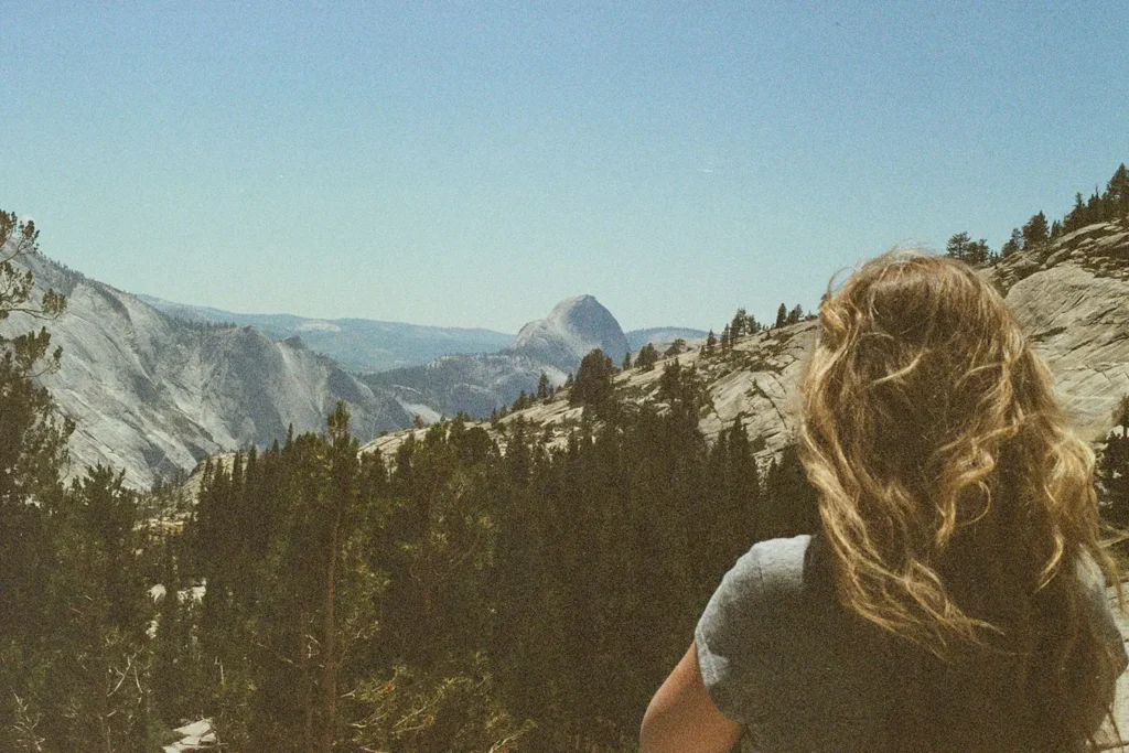 Woman with windblown hair looking out over a mountain landscape filled with pine trees and rugged cliffs