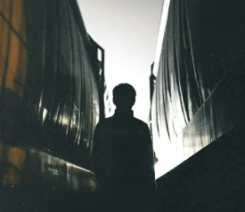 A silhouette of a person stands between two train cars in low light, with bright illumination behind them