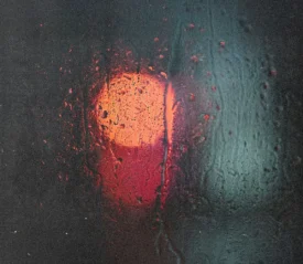 Blurred red and blue lights shining through a rain‑covered window