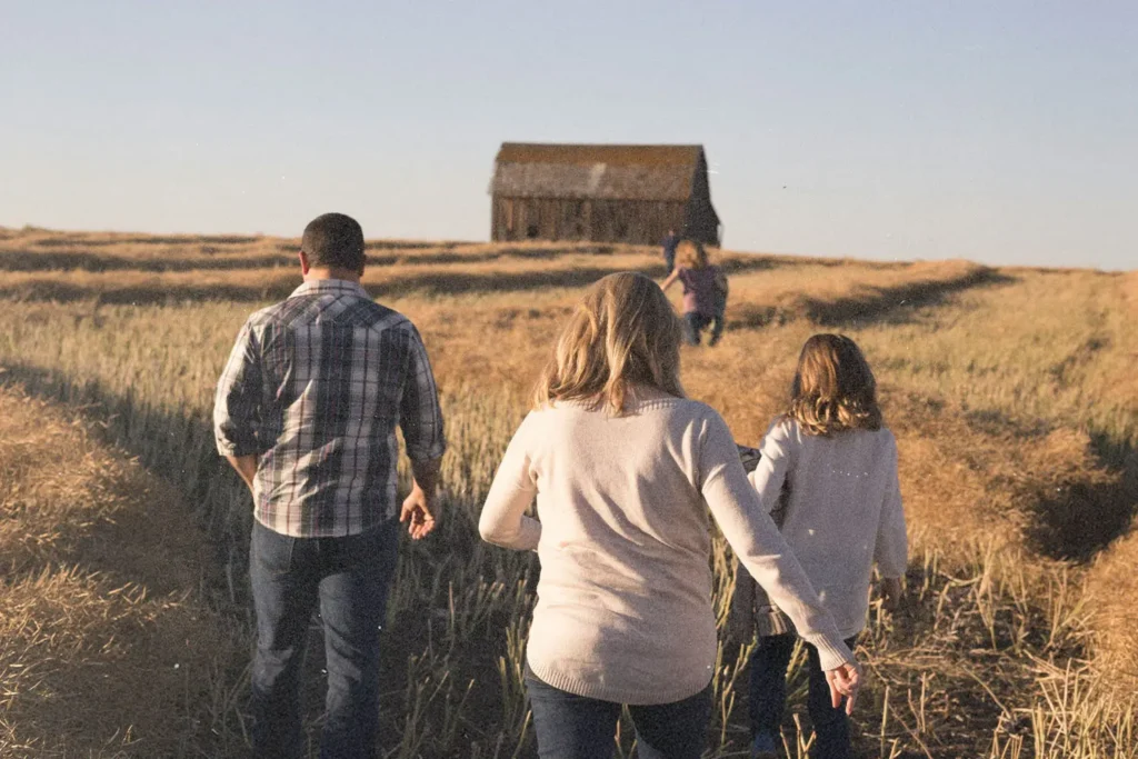 Group of people walking through a golden field toward an old wooden barn under a clear blue sky