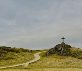 Hilltop cross rising above rolling grasslands beneath an overcast sky