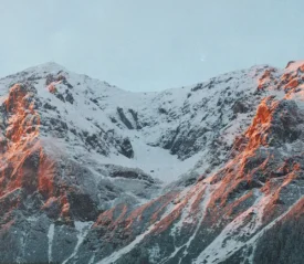 Snow‑covered mountain range illuminated by warm sunrise light along the rocky peaks