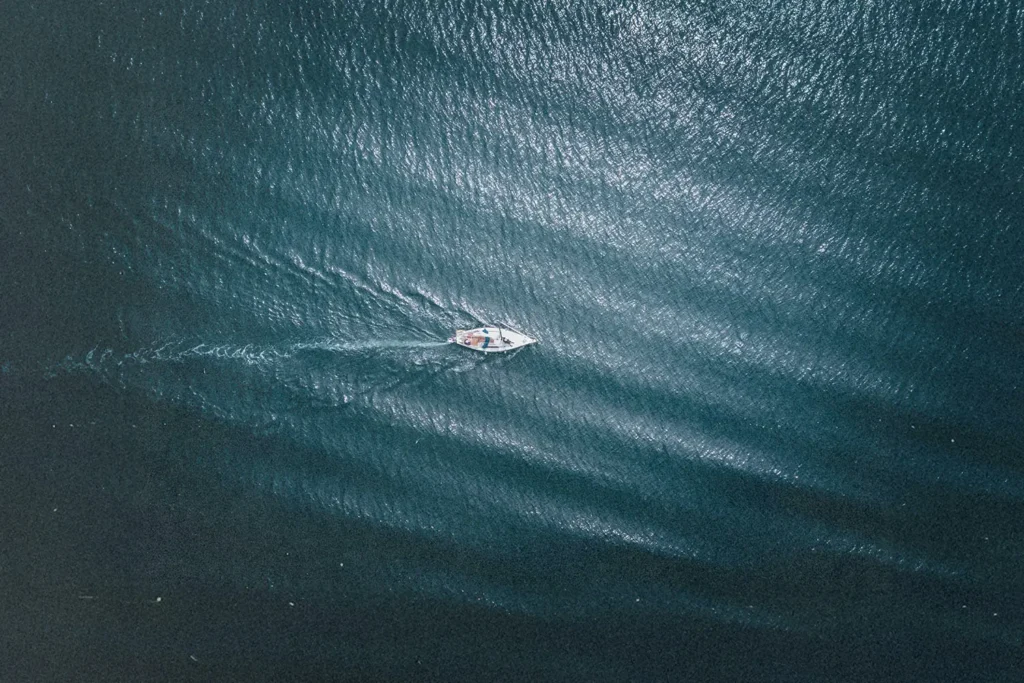 “Aerial view of a small boat moving across deep blue water, leaving a soft wake behind it