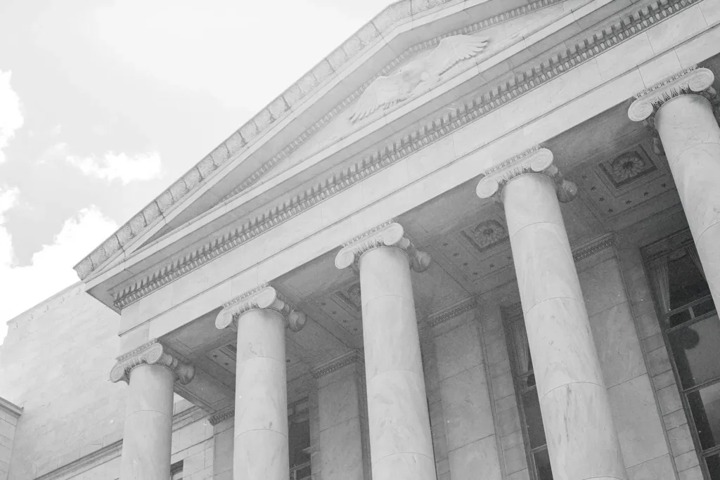 A stone building with tall columns and classical architecture is shown from a low angle, emphasizing its height and symmetry