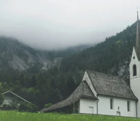 Small white church with a steeple set against foggy mountains and lush green hills