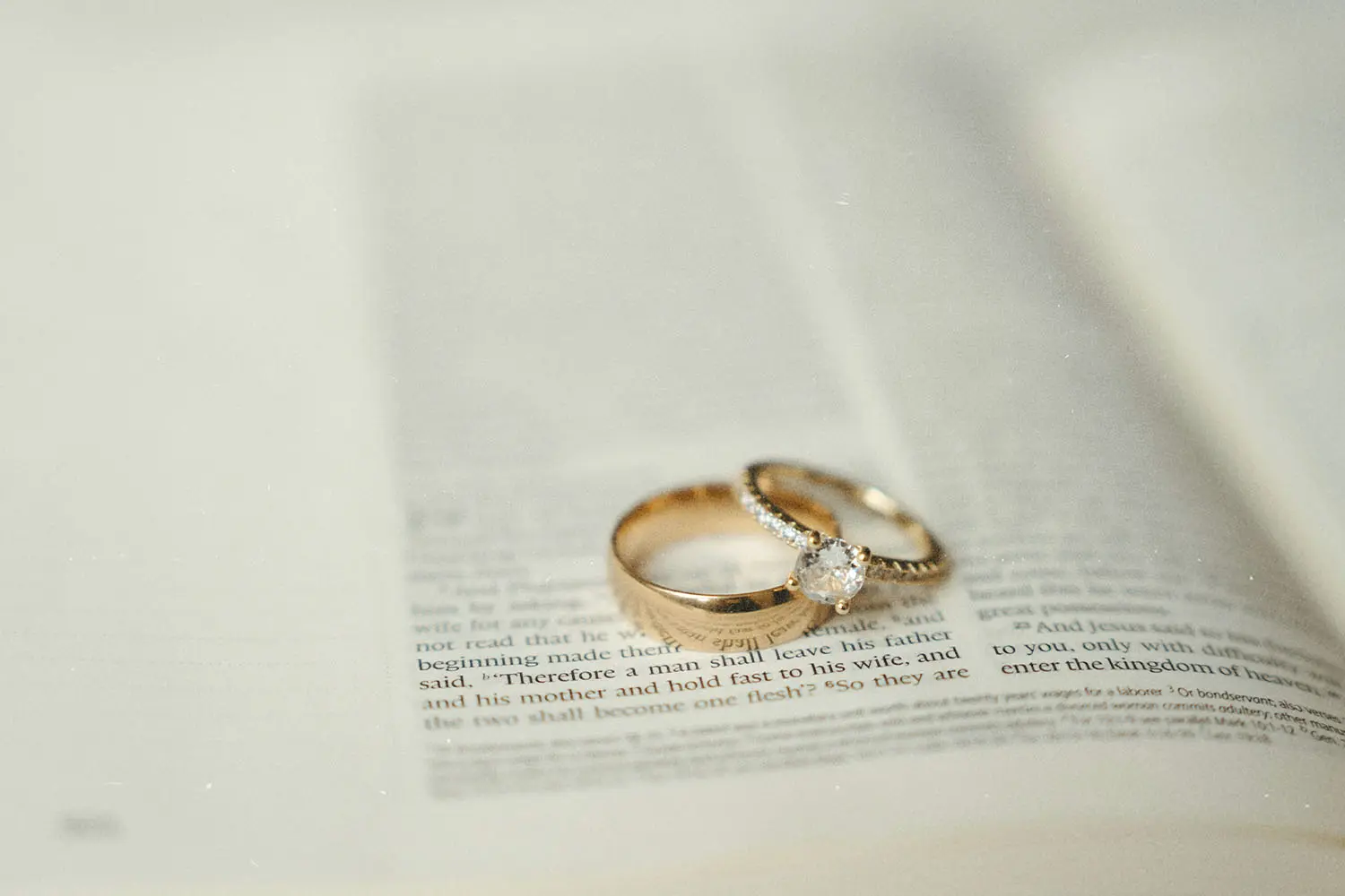 Two gold wedding rings, one with a diamond, rest on the open pages of a Bible