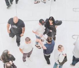 Group of people walking and interacting in a bright, modern indoor mall with white tile floors and metal railings