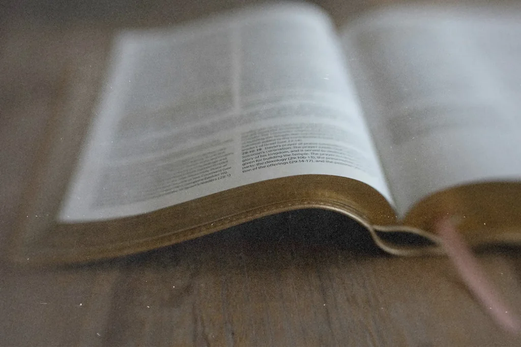 Open Bible resting on a wooden surface with pages slightly curved and soft natural light across the text