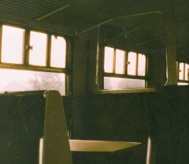 Empty train seats and sunlit windows inside an old-fashioned railway carriage, with warm light filtering through the glass