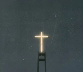 Illuminated cross glowing atop a tall church structure against a dark night sky
