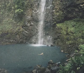 Waterfall flowing into a blue pool with a person swimming below