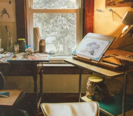 Cozy art studio with drawing desk, paints, and window light