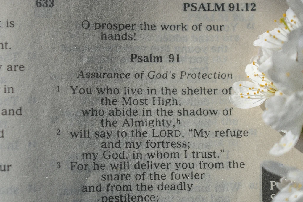 Close-up of an open Bible showing Psalm 91 with white flowers resting along the page edge