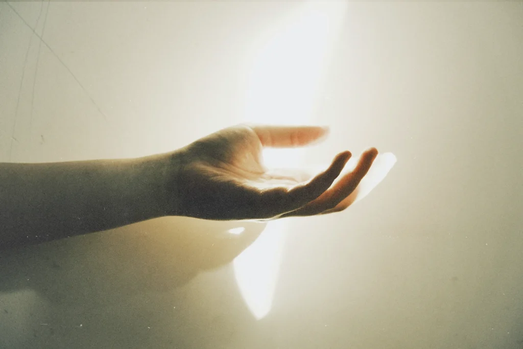 Outstretched hand reaching toward a bright beam of light against a softly lit wall