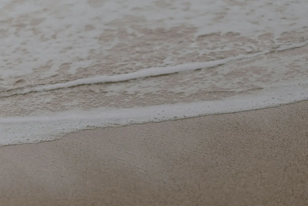 Gentle ocean waves roll onto smooth, wet sand in soft, muted lighting