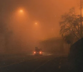 Vehicle driving through dense nighttime fog under glowing overhead lights