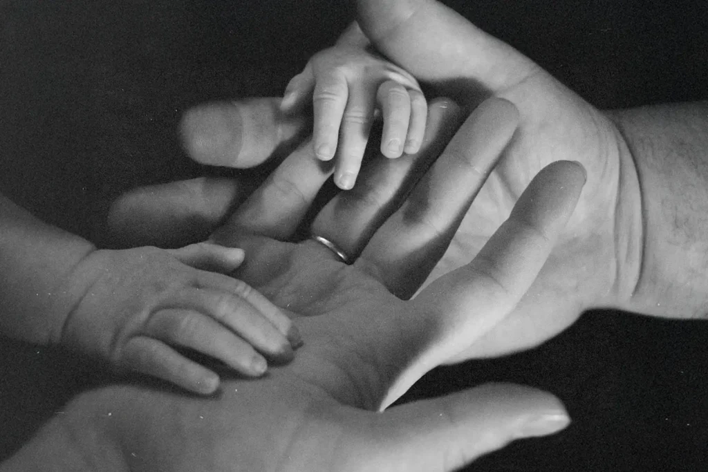 Close‑up of adult hands gently holding a baby’s hands