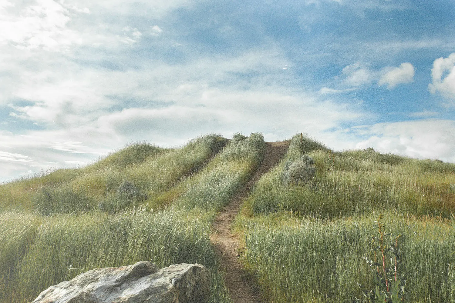 Dirt path leading through green grassy hills under a bright sky