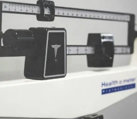 Close-up of a medical beam balance scale with measurement sliders and a caduceus symbol on the front