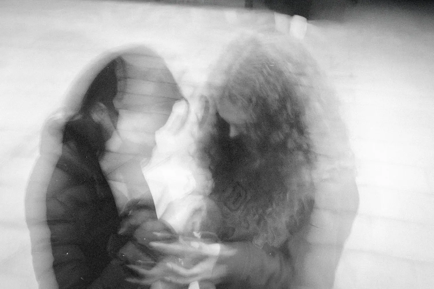 Two people sitting closely together in a soft, double‑exposed black‑and‑white image, creating a dreamy, motion‑blur effect