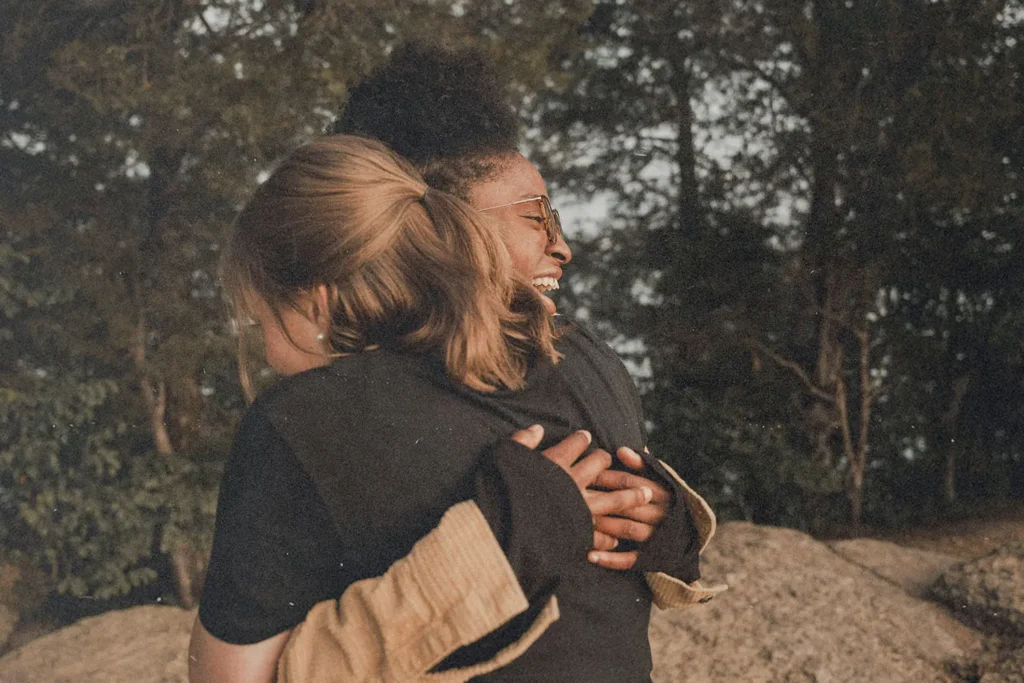 Two people embracing outdoors near large rocks, surrounded by trees and natural scenery