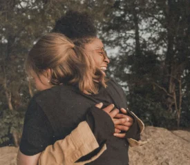 Two people embracing outdoors near large rocks, surrounded by trees and natural scenery