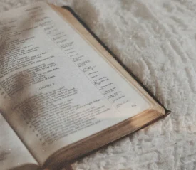 Open Bible resting on a soft white blanket with gentle light falling across the pages