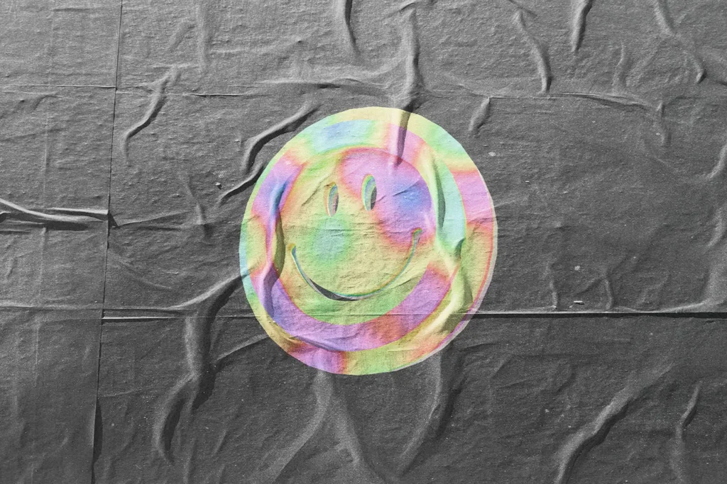 A colorful, iridescent smiley face graphic printed on a wrinkled dark fabric background