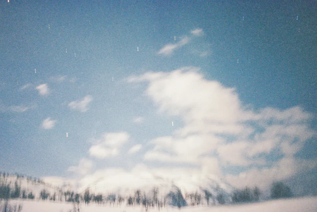 A snowy landscape stretches across the scene under a bright, cloud‑filled sky with faint streaks of stars above