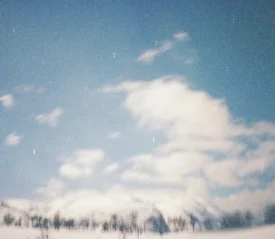 A snowy landscape stretches across the scene under a bright, cloud‑filled sky with faint streaks of stars above