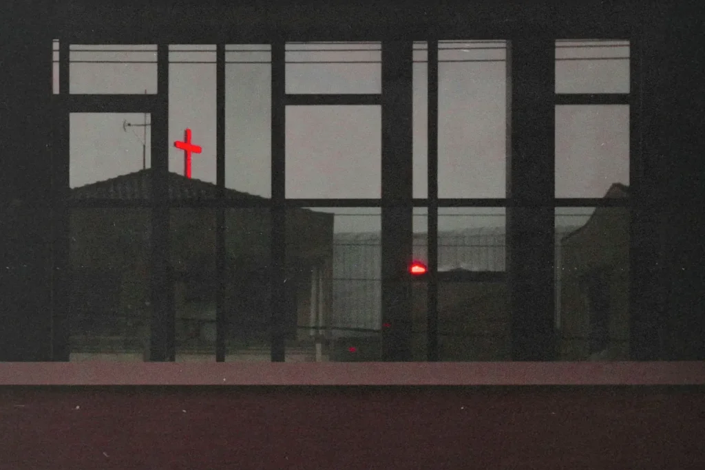 View from a window of a neon red cross atop a building in the distance