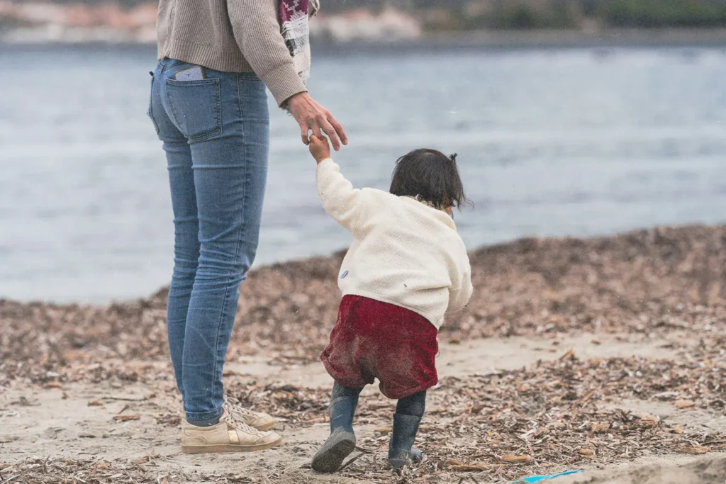 Woman holding the hand of a child walking on the shore