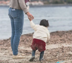 Woman holding the hand of a child walking on the shore